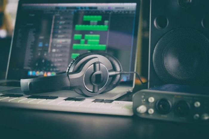 Studio setup with headphones, keyboard, and computer for music production. Mixing software visible on screen.