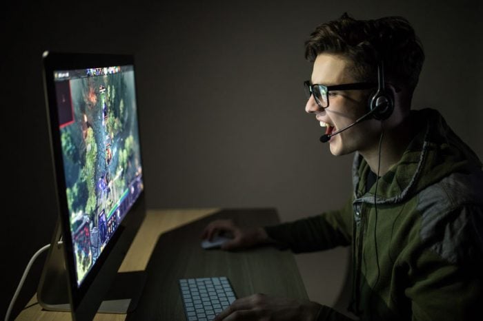 Gamer enthusiastically playing a strategy game on PC with headset, focused and engaged in a dark room.