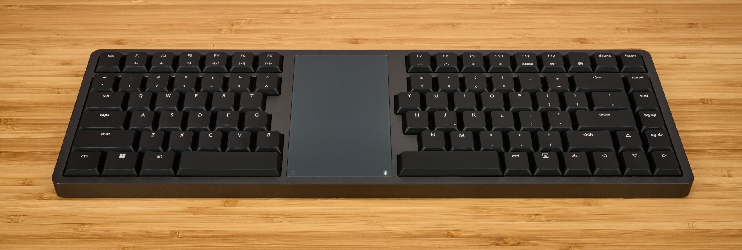 Modern black keyboard with integrated touchpad on wooden desk. Ideal for efficient computing and minimalistic workspace.