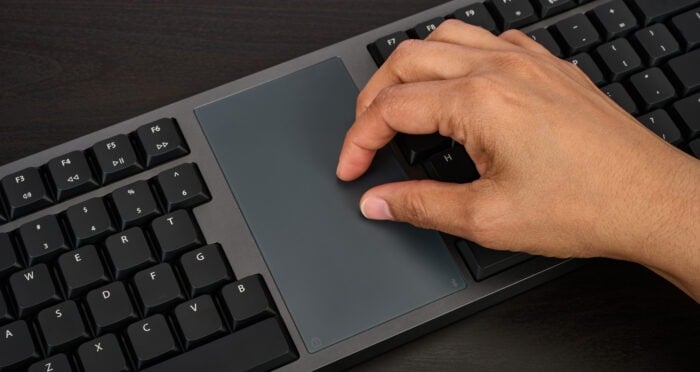 Hand using a touchpad on a black keyboard, demonstrating modern computer interaction.