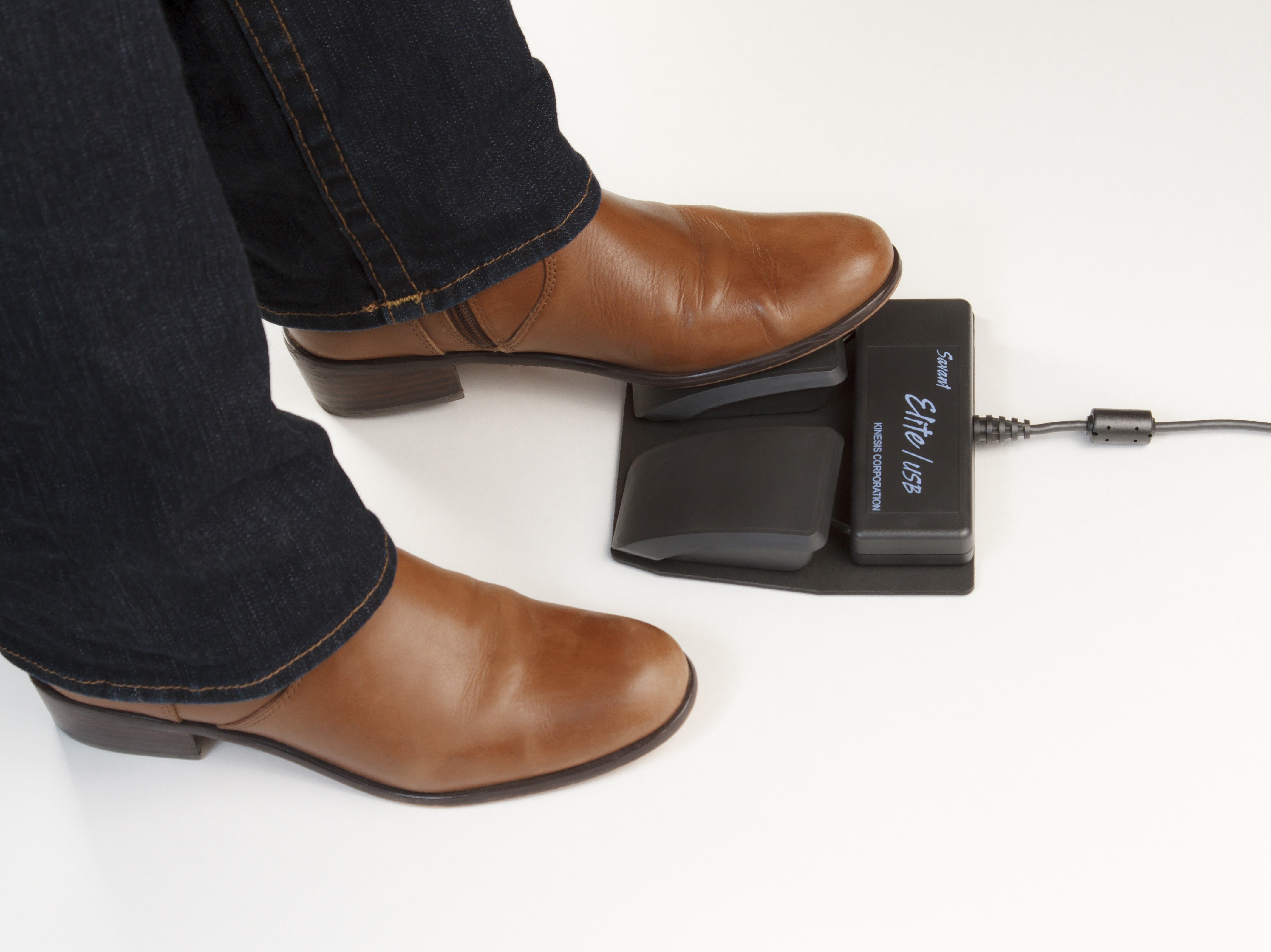 Person operating a foot pedal control with brown boots, connected via USB for hands-free computer tasks.