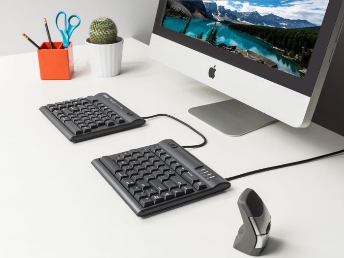 Ergonomic split keyboard and vertical mouse setup with monitor on modern white desk.