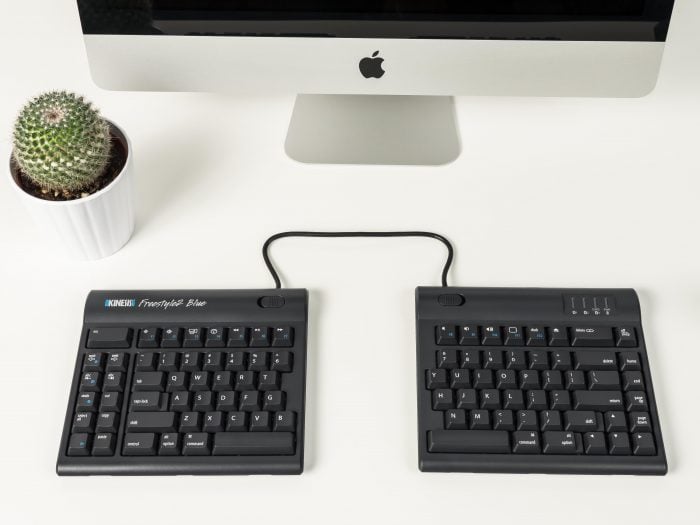 Ergonomic split keyboard on a desk with an iMac and potted cactus, optimizing workspace comfort and functionality.