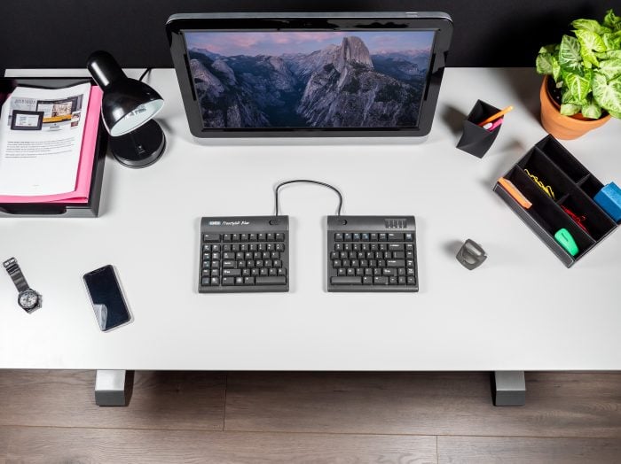 Modern workspace with ergonomic split keyboard, monitor, and organized accessories on a sleek white desk.