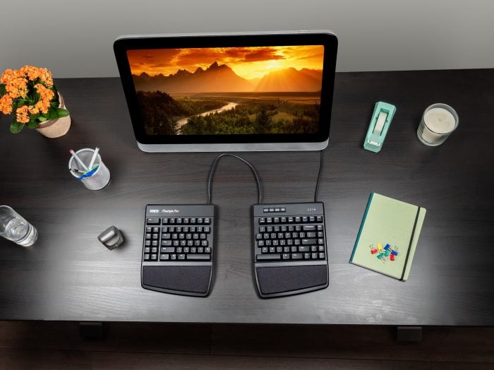 Ergonomic split keyboard setup with a scenic landscape on screen, surrounded by office supplies on a modern desk.