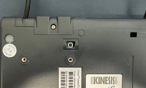 Close-up view of a Kinesis device's underside, featuring a screw insert and model details on a label.