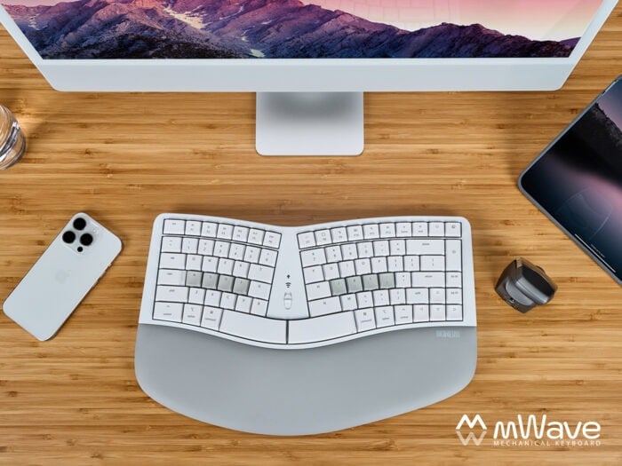 Ergonomic mechanical keyboard setup with monitor, phone, and tablet on a wooden desk for efficient workspace.