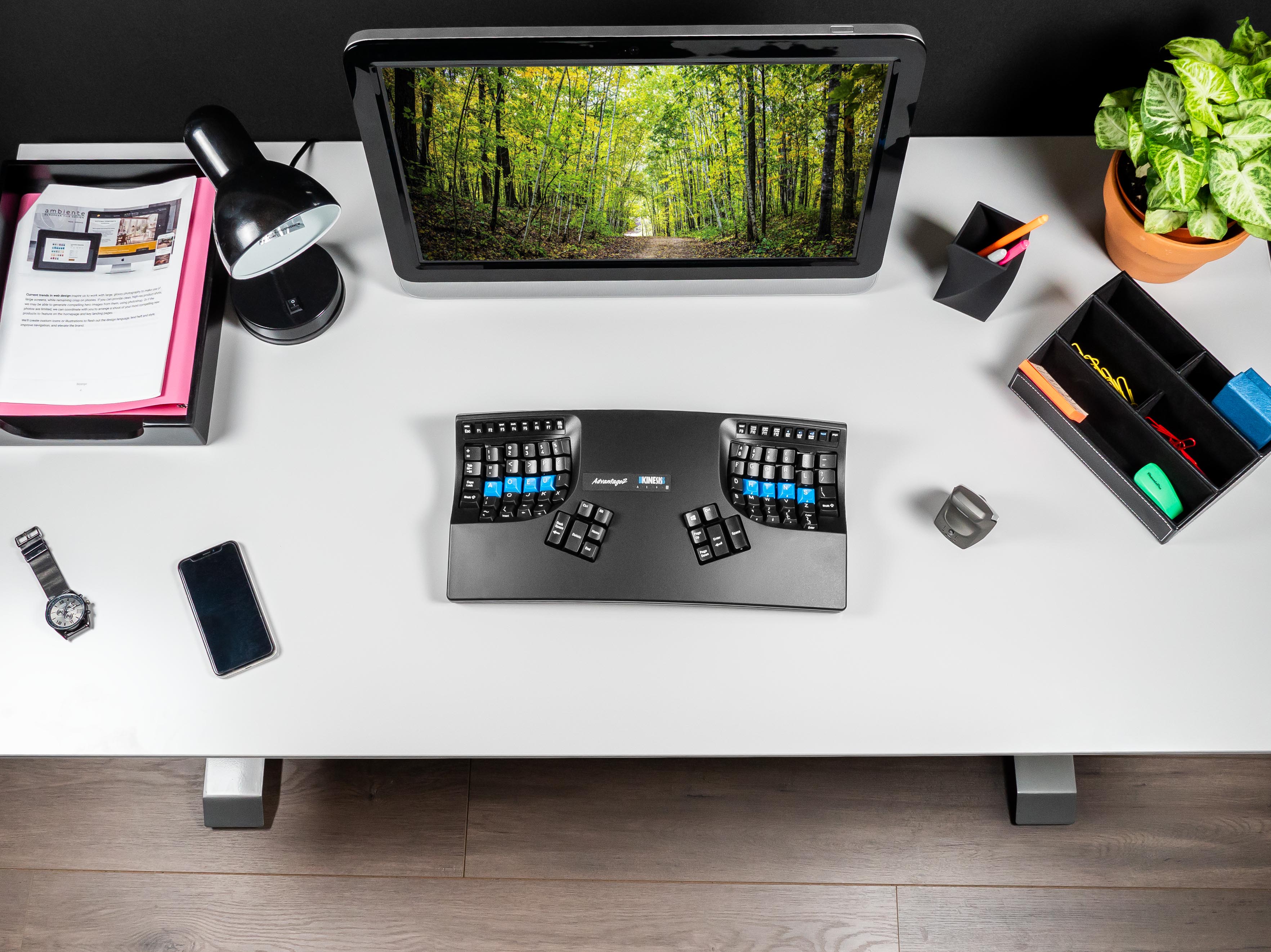 Ergonomic keyboard on a modern desk with monitor, lamp, phone, and office supplies for a productive workspace.