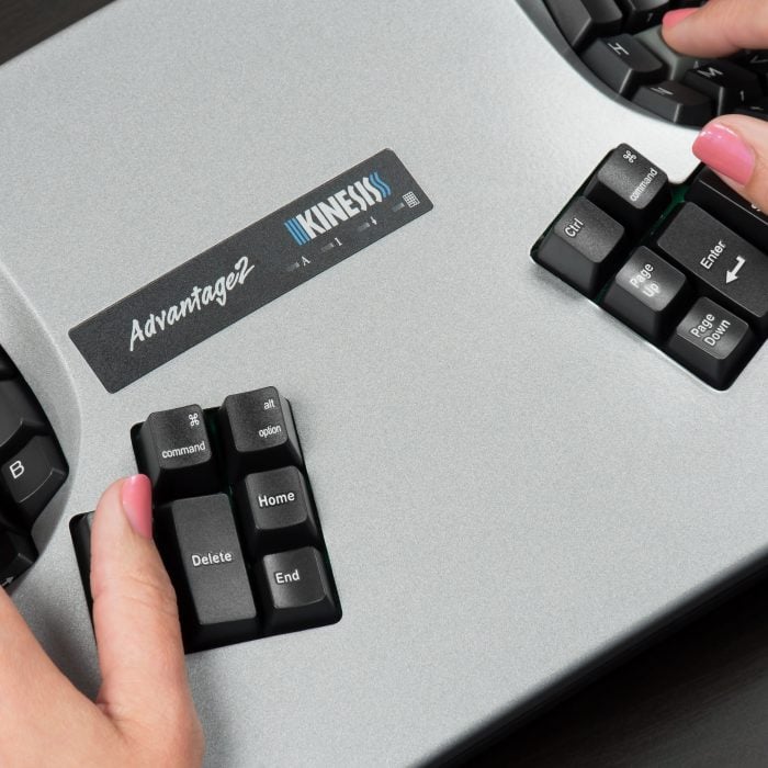 Close-up of hands typing on a silver Kinesis Advantage2 ergonomic keyboard with black keys.