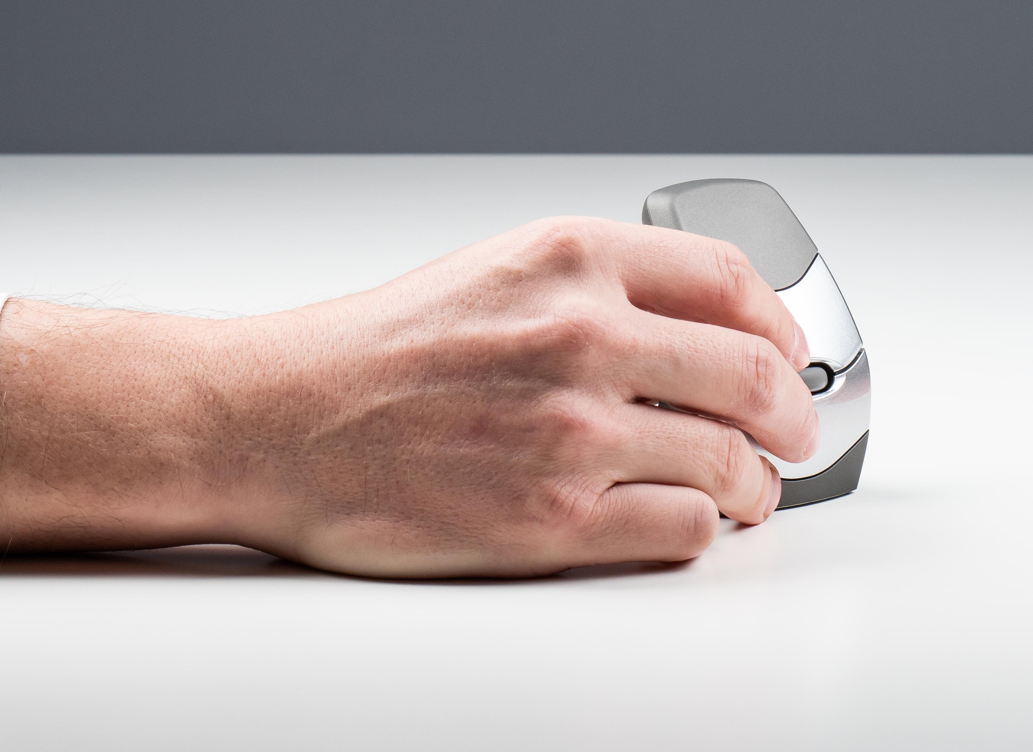 Hand holding an ergonomic mouse on a white desk, emphasizing comfort and efficient design for computer use.