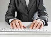Professional typing on keyboard, close-up of hands, business attire, office work environment.