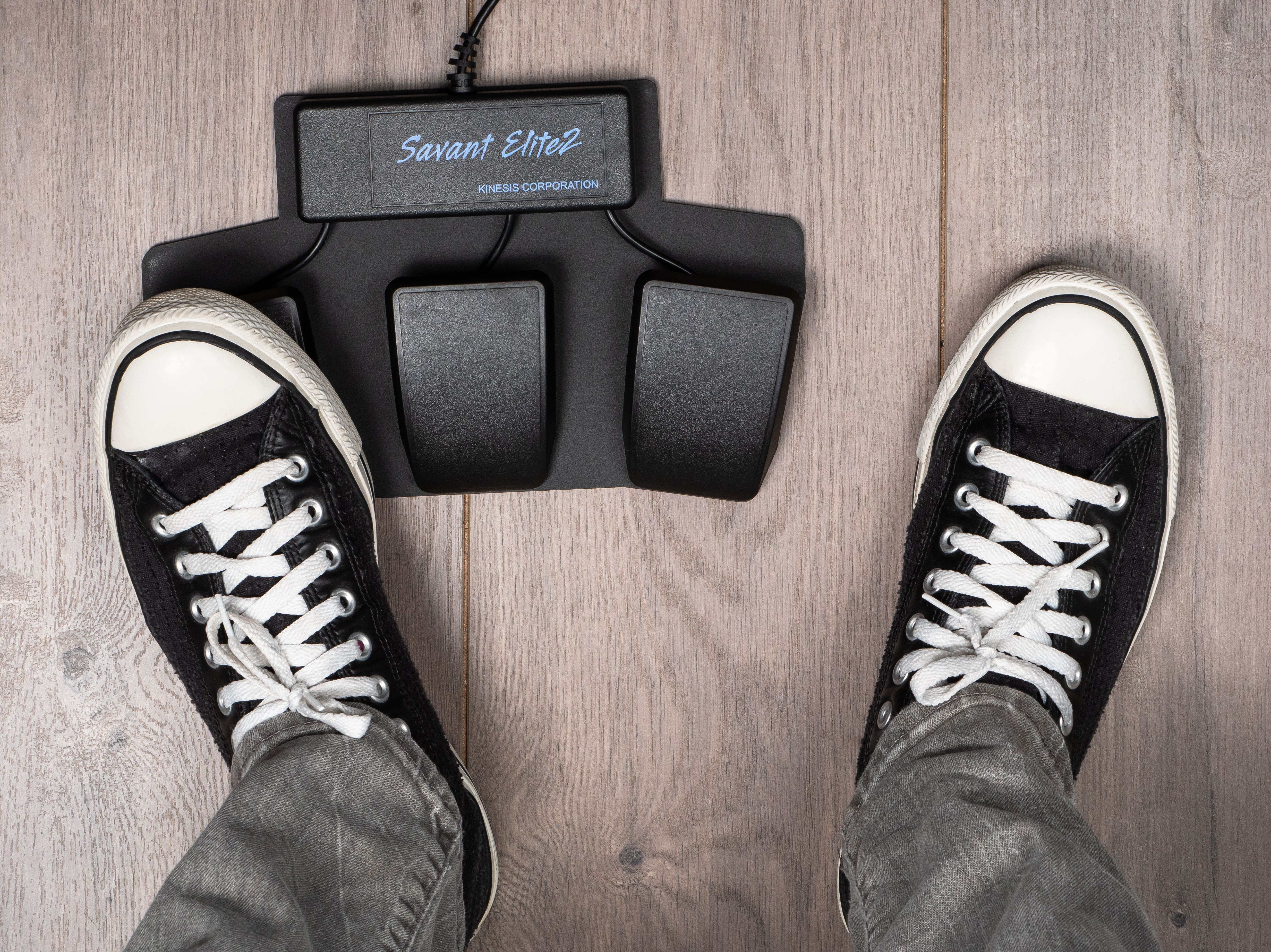Black sneakers operating a Savant Elite2 foot pedal on a wooden floor.