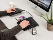 Ergonomic dual keyboard setup with a computer and smartphone on a desk, featuring a candle and aloe plant for aesthetics.