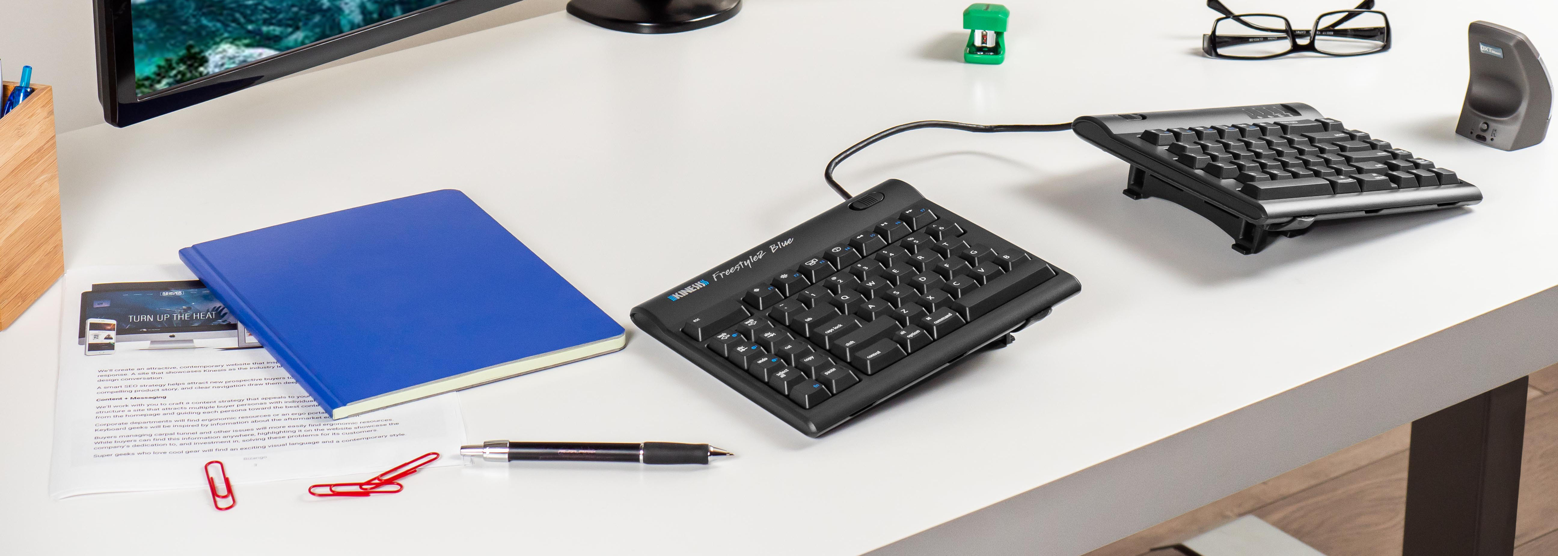 Ergonomic split keyboard on desk with notebook and office supplies for a comfortable workspace setup.