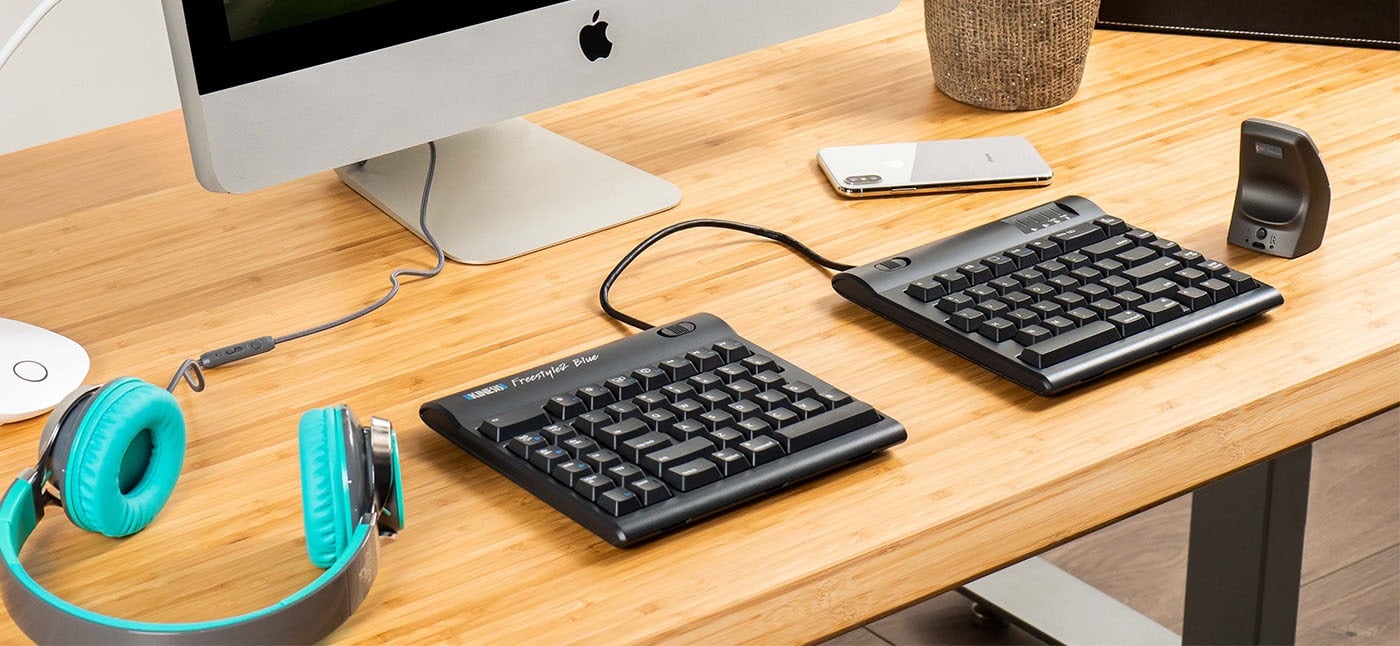 Dual ergonomic split keyboards on a wooden desk with Mac, headphones, and smartphone.