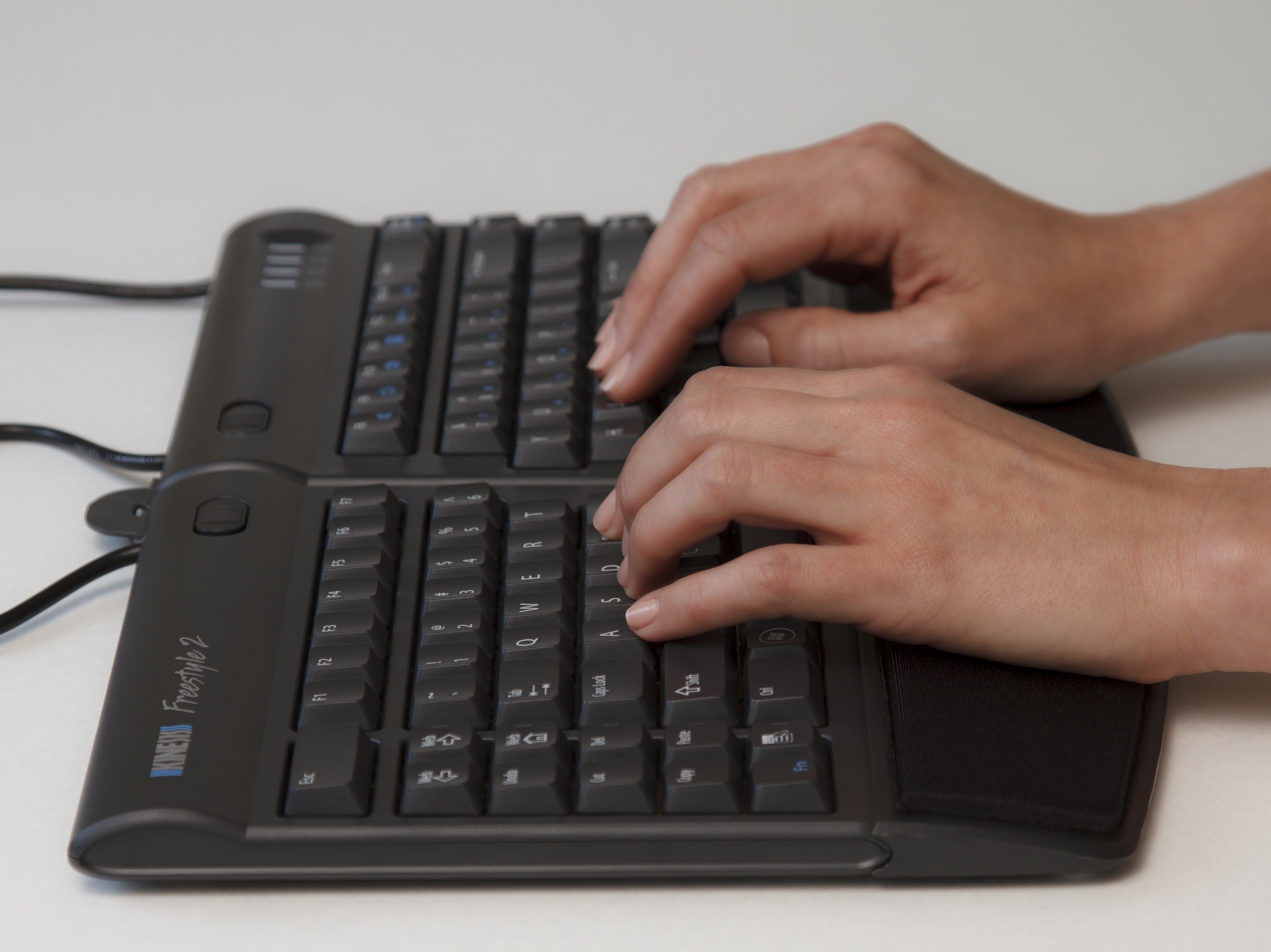 Hands typing on a split ergonomic keyboard, enhancing comfort and efficiency in computer use.