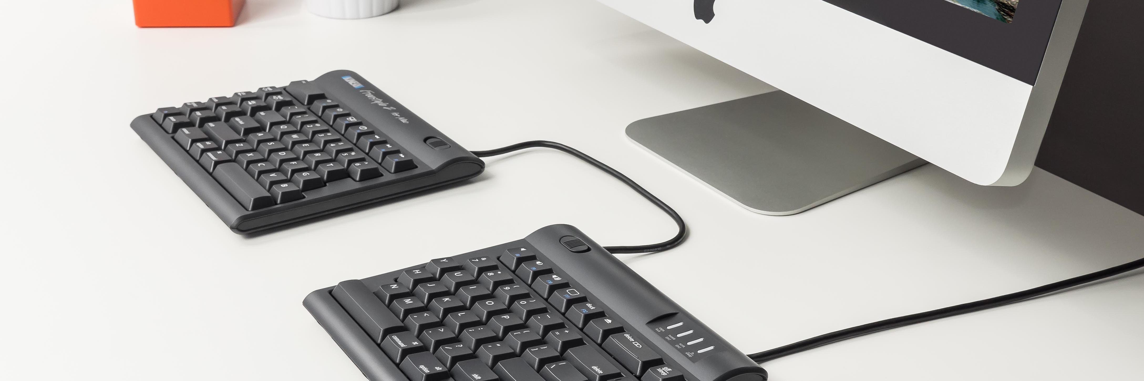 Ergonomic split keyboard connected to desktop computer on a modern white desk, enhancing workspace comfort.
