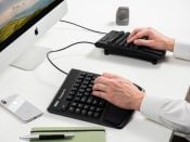 Ergonomic split keyboard setup on desk with computer, smartphone, and notepad for efficient workspace organization.