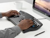 Person typing on an ergonomic keyboard at a desk with a computer, coffee mug, and pen nearby.
