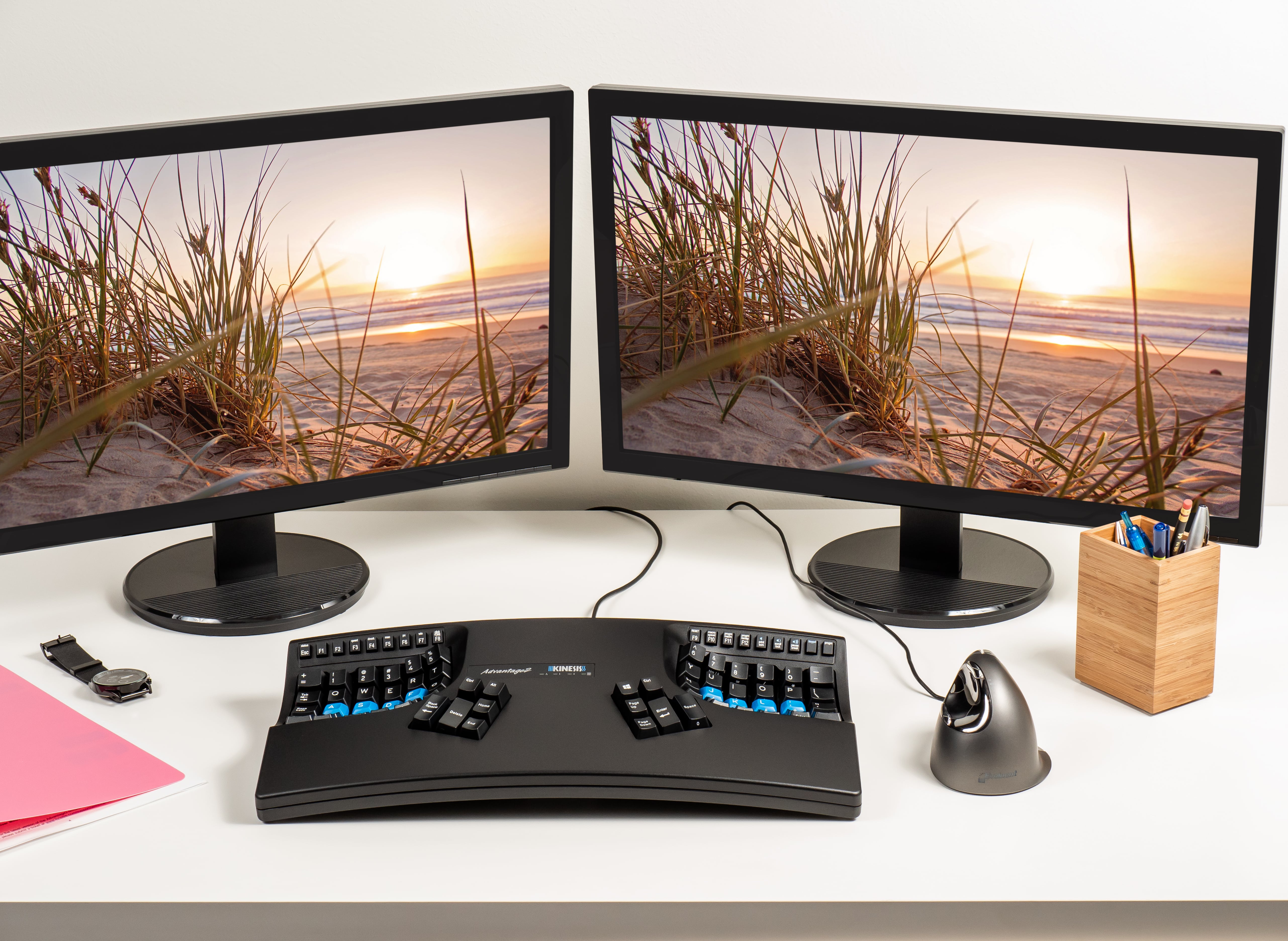Dual monitor setup with ergonomic keyboard and vertical mouse on a desk. Beach scene on screens for productivity.