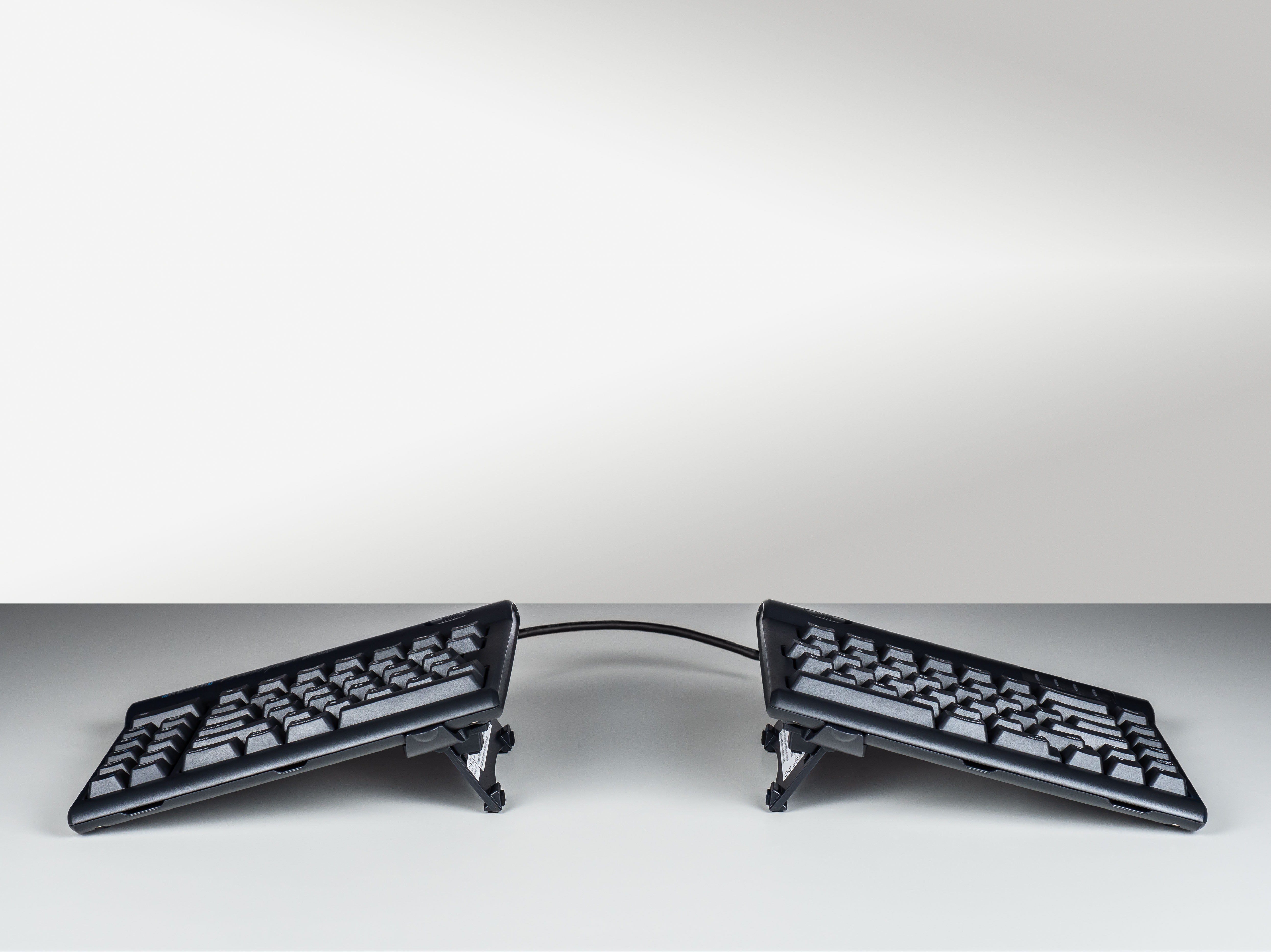 Ergonomic split keyboard with adjustable stands for comfortable typing, connected by a flexible cable on a white background.