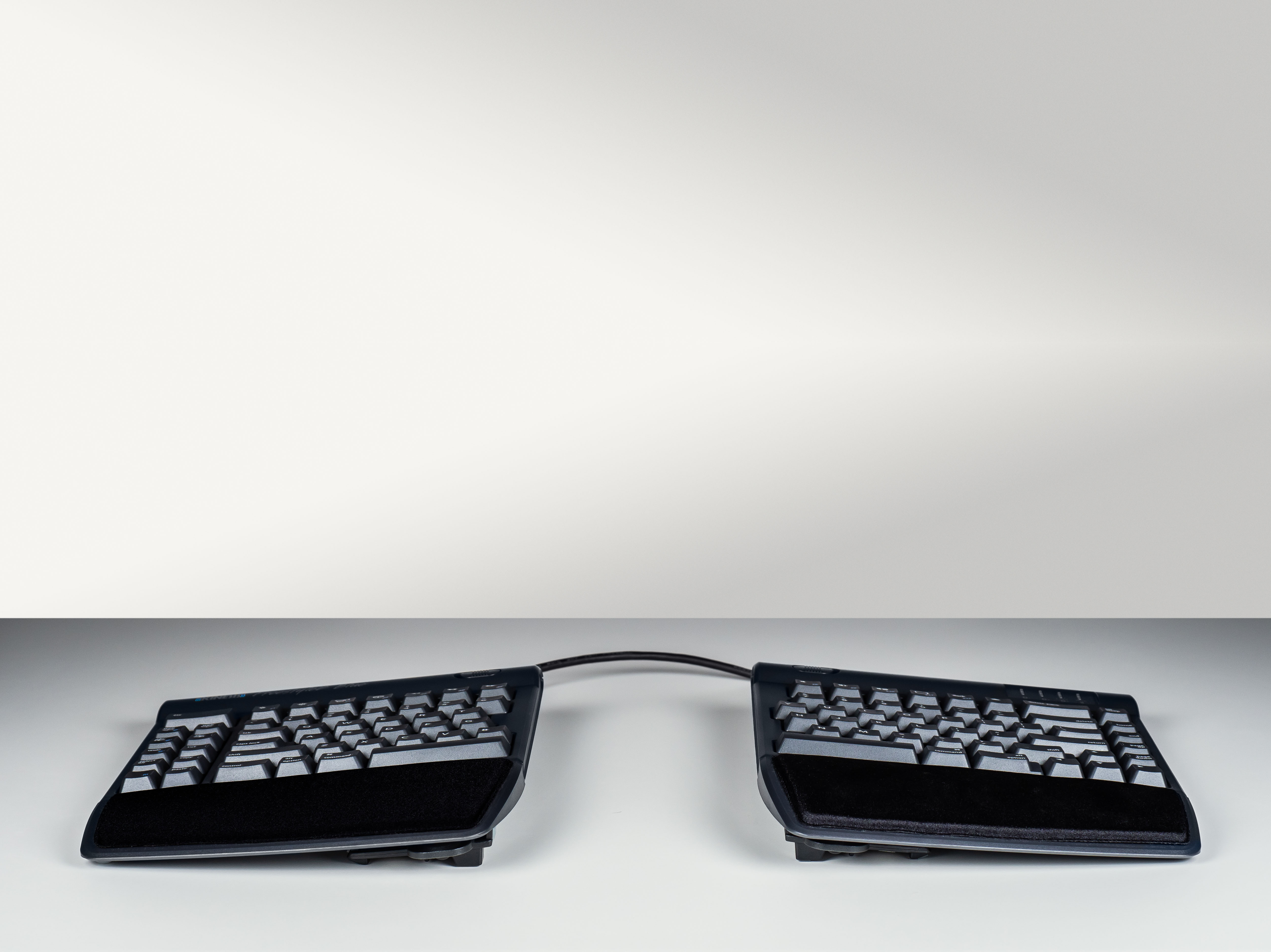 Ergonomic split keyboard with wrist rests on a gray background for comfortable typing.