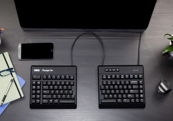 Ergonomic split keyboard setup with smartphone and notebook on a sleek desk. Ideal for comfortable typing.