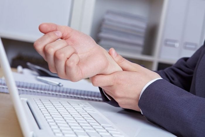 Person holding wrist in pain at computer keyboard, indicating potential office-related strain or injury.