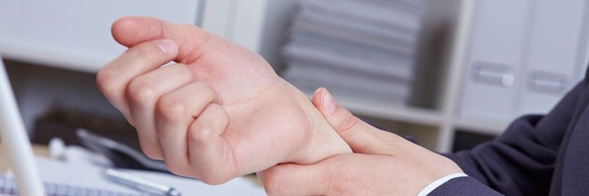 Person holding wrist in pain, office setting, ergonomic issues, workplace injury prevention, health and safety awareness.