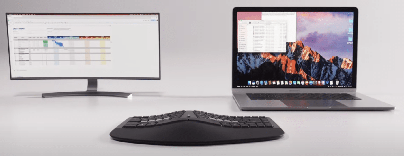 Ergonomic keyboard with widescreen monitor and laptop displaying digital workspace, enhancing productivity setup.