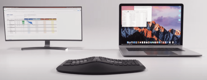 Ergonomic keyboard with widescreen monitor and laptop displaying digital workspace, enhancing productivity setup.