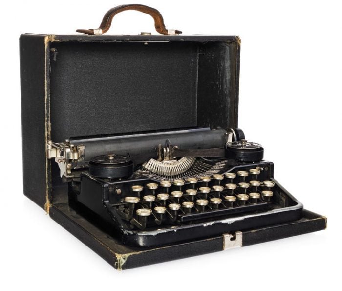 Vintage typewriter in an open black case, showcasing keys and paper feed, symbolizing classic writing tools.