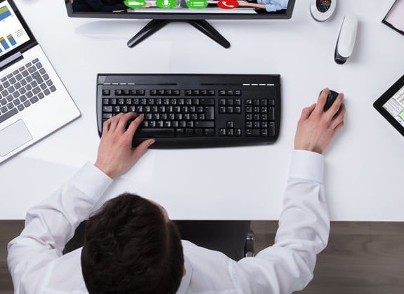 Overhead view of person using a computer mouse and keyboard at an office desk with a monitor.