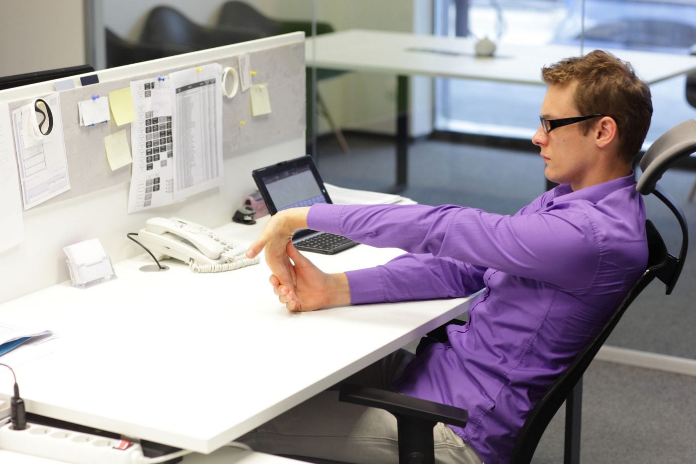 Office worker stretching hand at desk for ergonomic wellness.