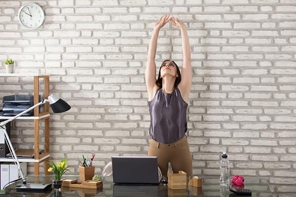Woman stretching at office desk for better posture and relaxation during work.