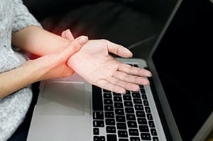 Person holding wrist in pain while using a laptop, highlighting repetitive strain injury from computer use.